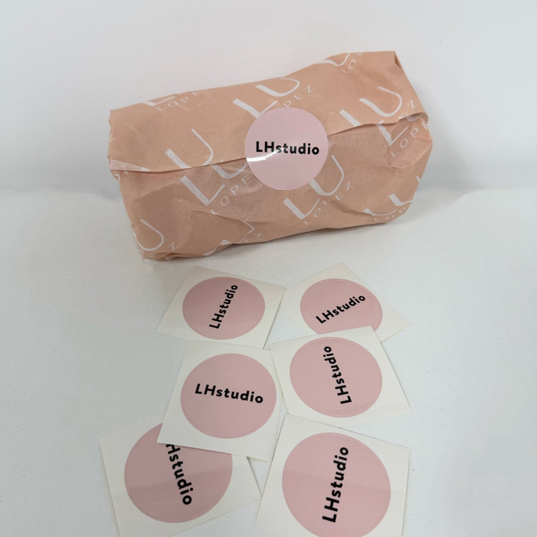 Coated paper round logo stickers scattered beside a wrapped product, glossy coated finish