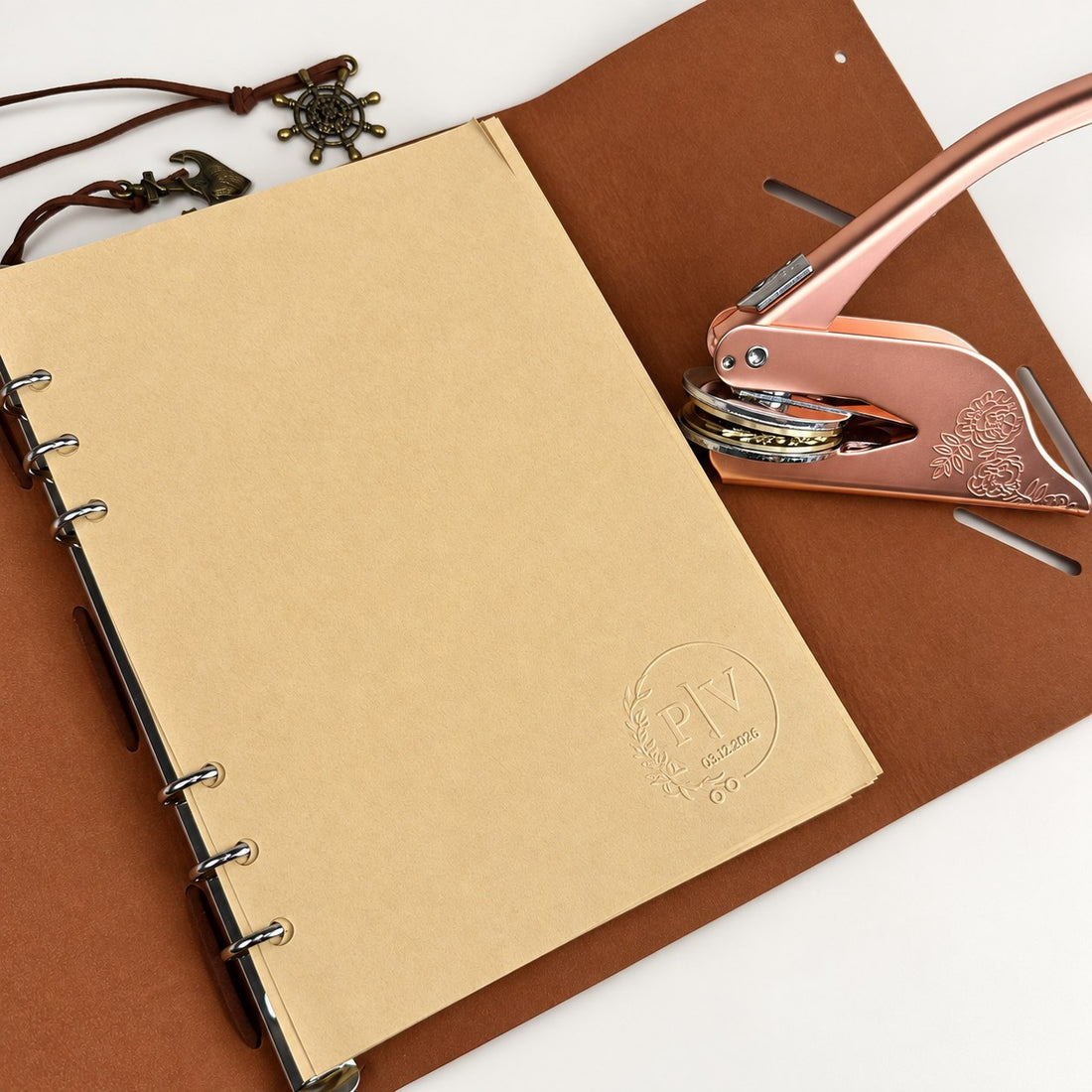 A kraft journal page embossed with a monogram seal beside a rose gold embosser