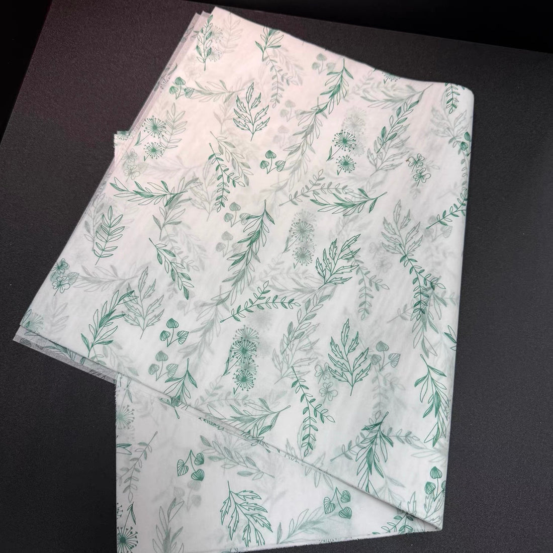 Folded stack of 17gsm custom tissue paper sheets printed with a green botanical pattern