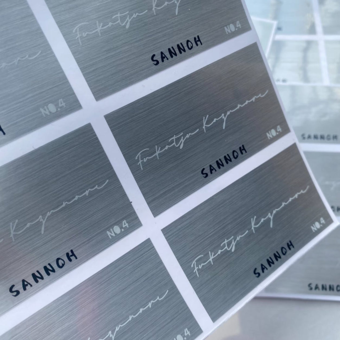 Sheet of brushed silver metallic rectangle stickers with a minimalist logo, premium metallic labels