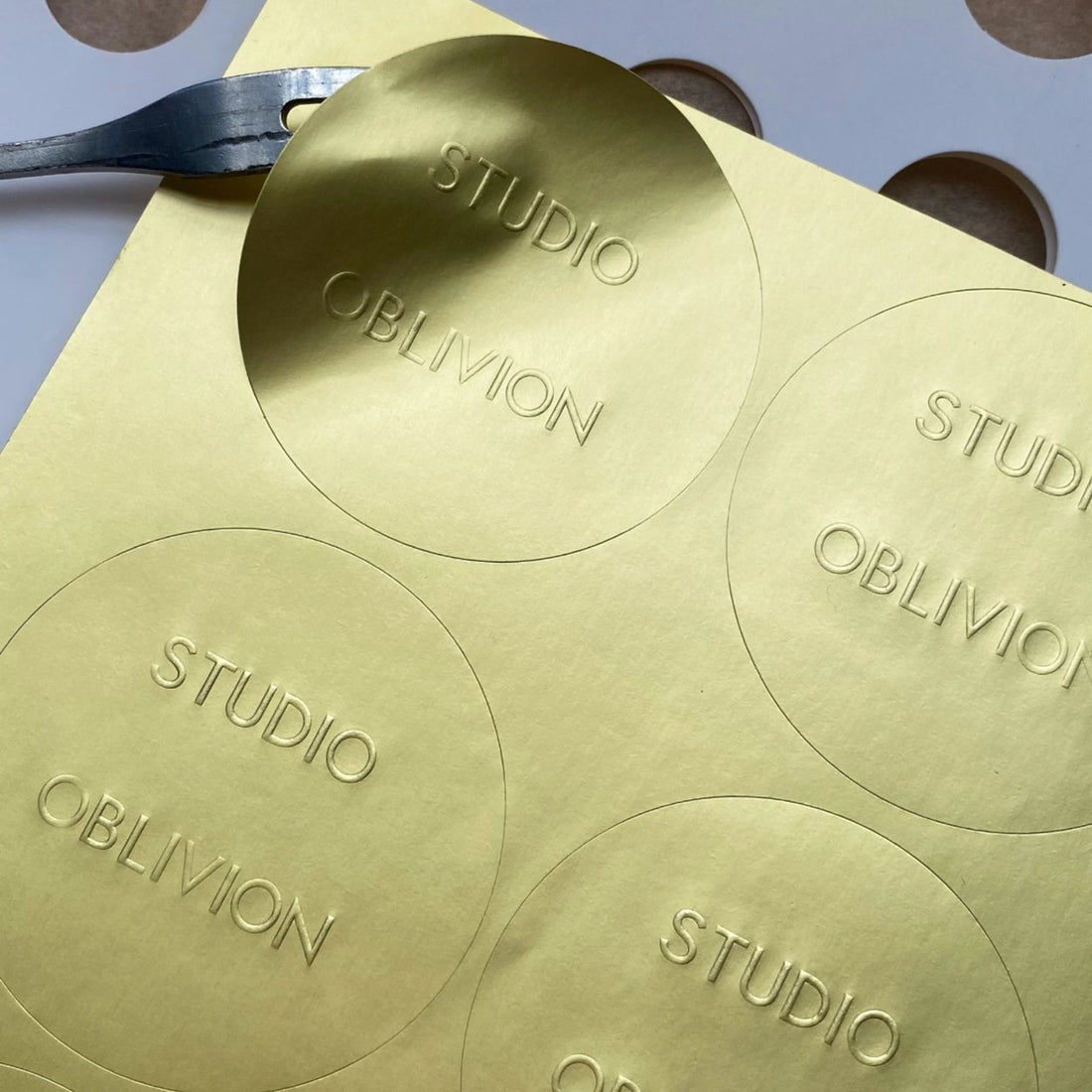 Gold brushed metallic circle stickers with a studio logo on a kiss-cut sheet, premium metallic finish