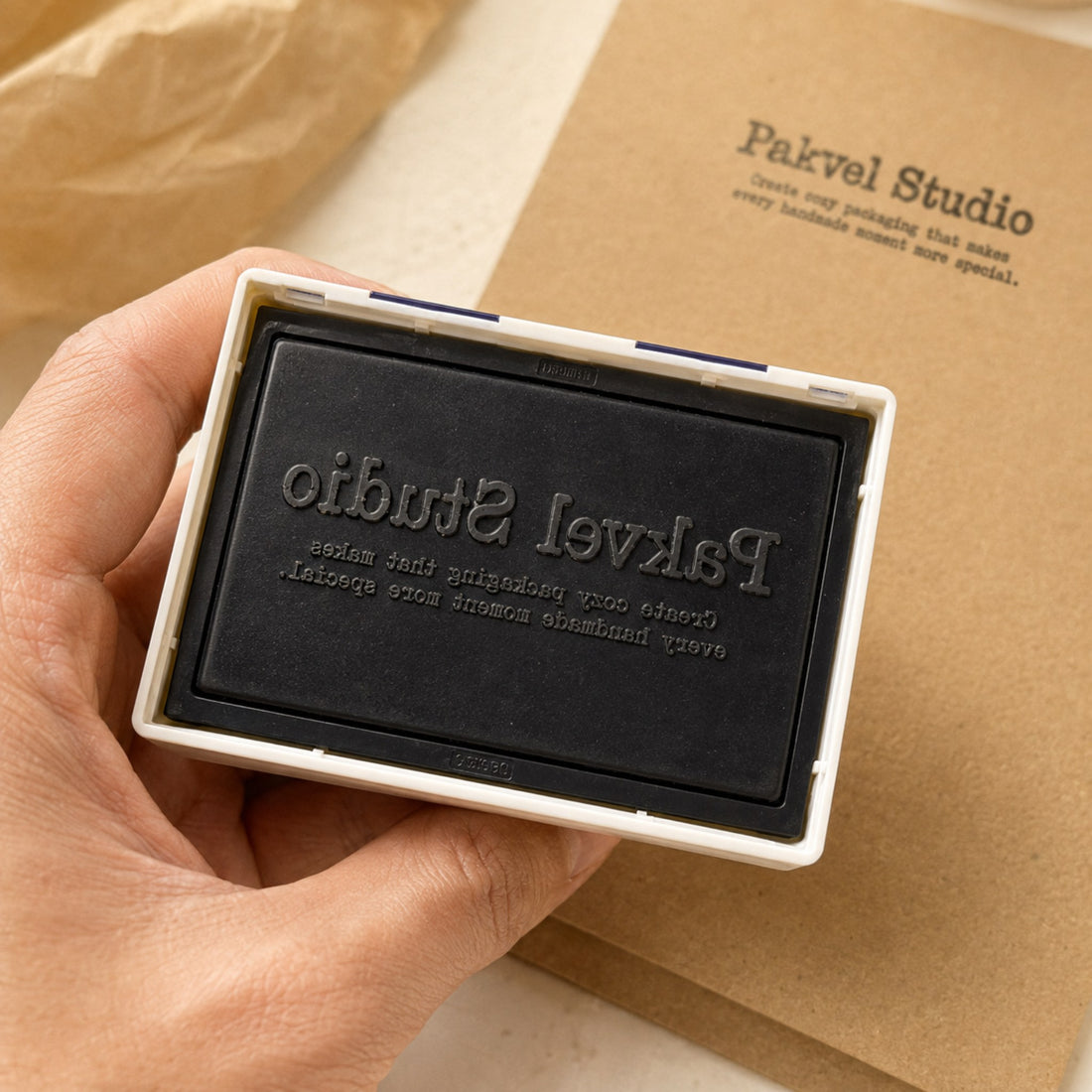 A hand holding a custom pre-inked stamp with the die exposed, showing the ink is held in the die itself with no separate ink pad