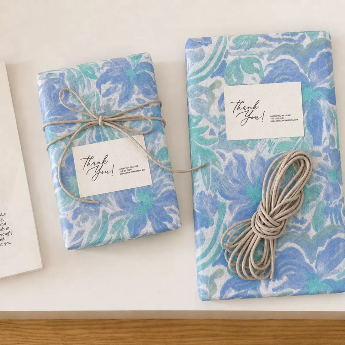 Gifts wrapped in blue floral tissue paper tied with cord and a thank-you card