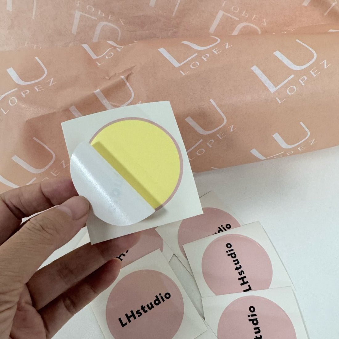 Hand peeling a round coated paper sticker from its backing, glossy coated kiss-cut label