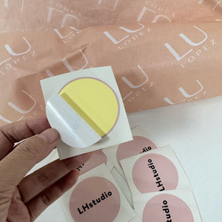 Hand peeling a round coated paper sticker from its backing, glossy coated kiss-cut label