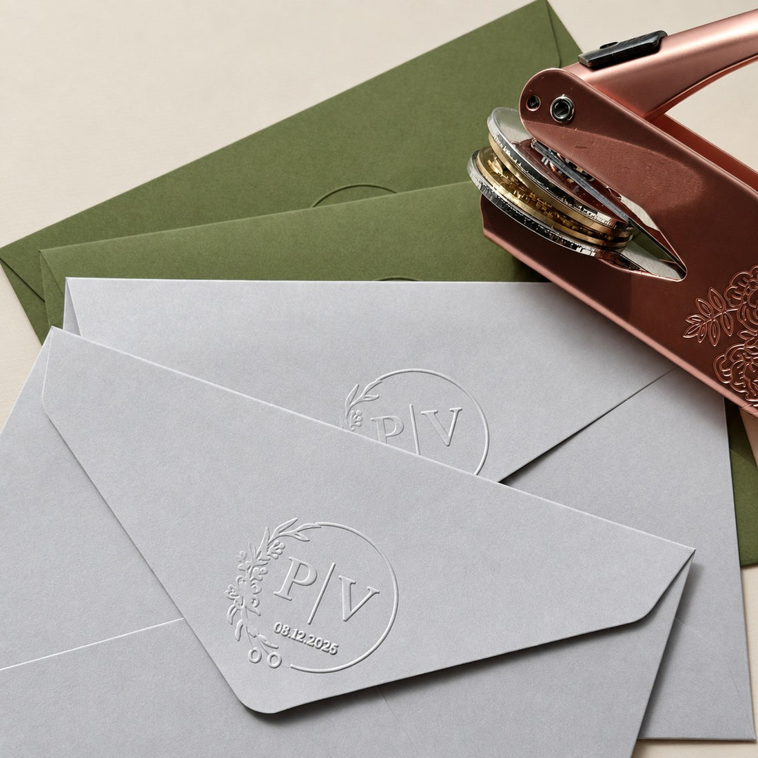 Grey and green envelopes embossed with a monogram seal beside a rose gold embosser