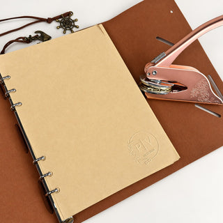 A kraft journal page embossed with a monogram seal beside a rose gold embosser