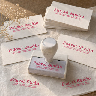 Custom pre-inked stamp inked in pink, with its impressions on cards and tissue paper beside dried flowers