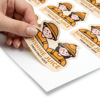 Hand peeling a custom die-cut matte paper character sticker from a kiss-cut sheet, full-color matte print