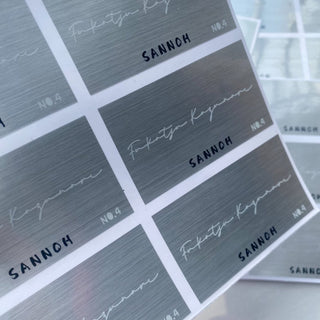 Sheet of brushed silver metallic rectangle stickers with a minimalist logo, premium metallic labels