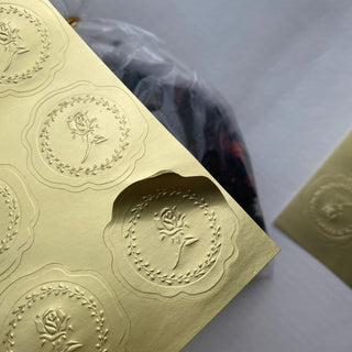 Custom die-cut gold metallic sticker with an embossed floral crest and scalloped edge