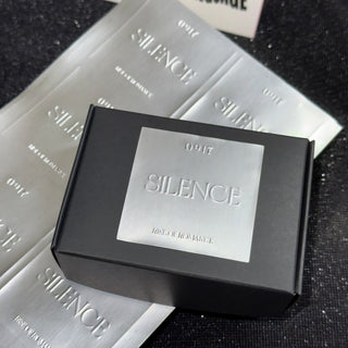 Matte silver embossed metallic label on a black gift box, raised deboss on matte silver foil