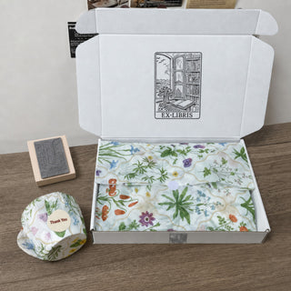 A white mailer box stamped with a logo, lined with printed tissue and sealed with a Thank You sticker