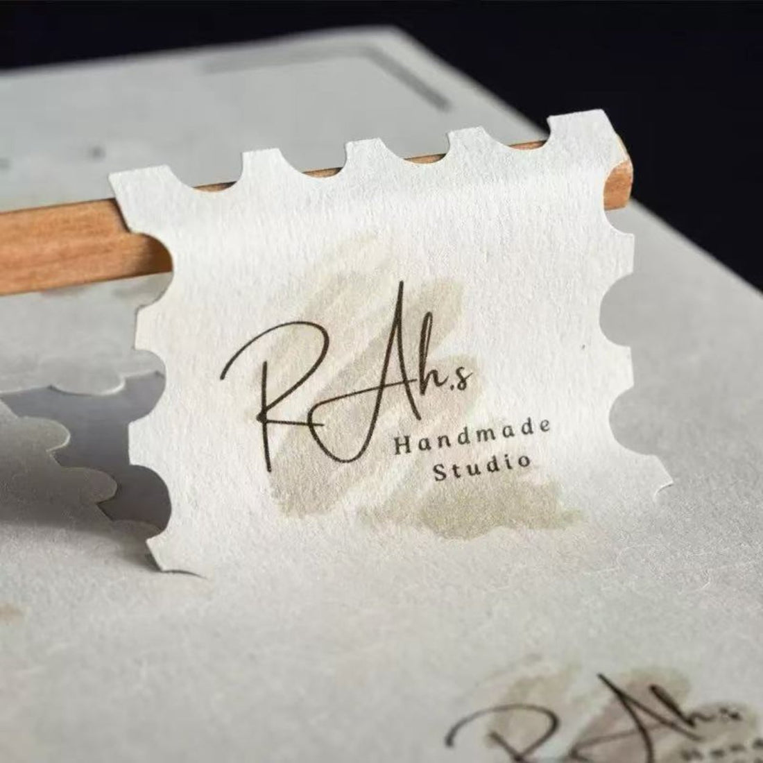 Custom die-cut textured paper sticker with a stamp-edge border and handmade studio logo, embossed kraft texture