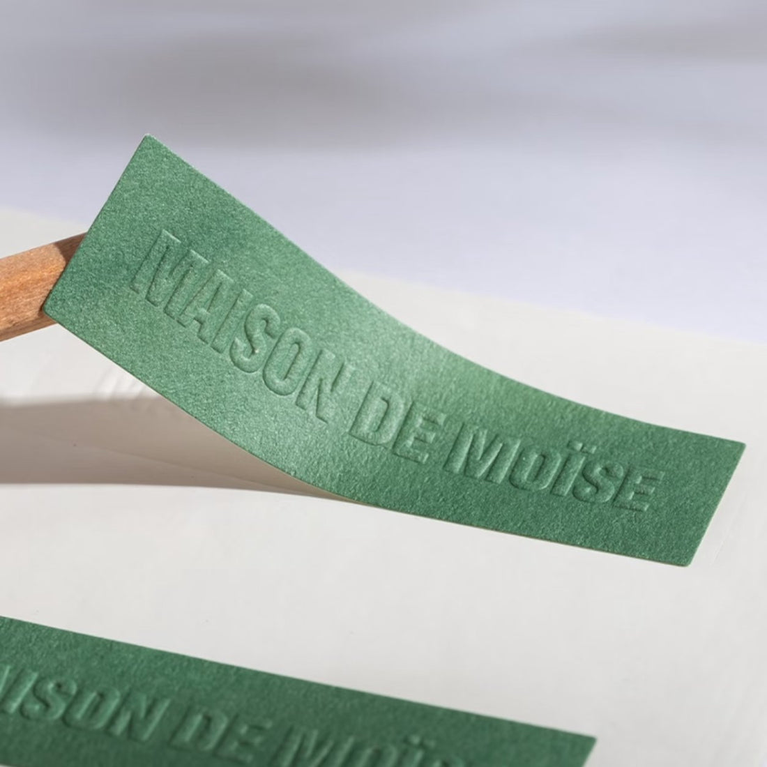 Green textured paper label with embossed and debossed lettering, premium tactile finish