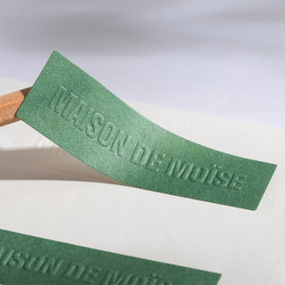 Green textured paper label with embossed and debossed lettering, premium tactile finish