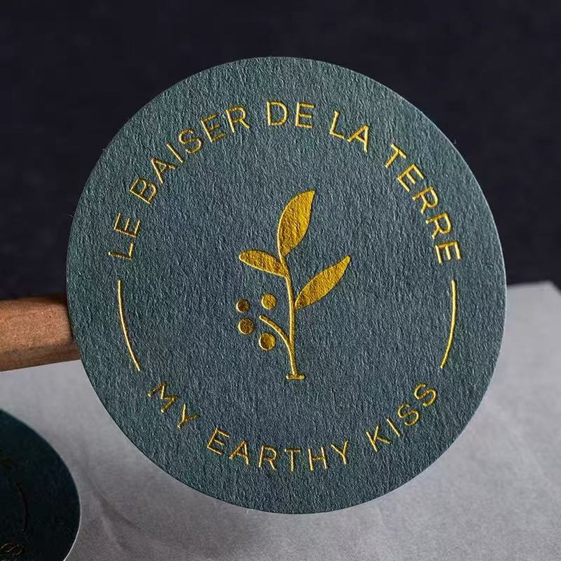 Dark teal textured paper sticker with a gold foil leaf emblem, metallic foil on felt-textured paper