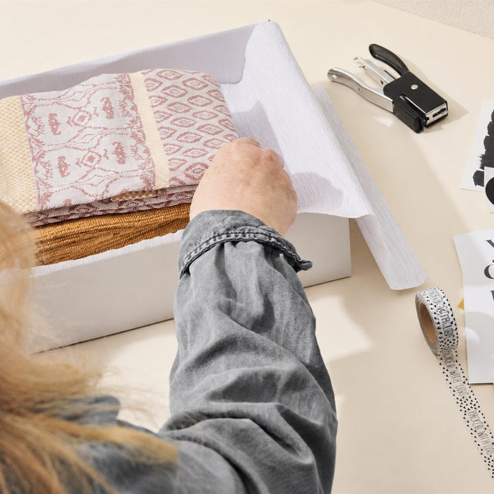 Handmade textiles being wrapped in tissue inside a shipping box