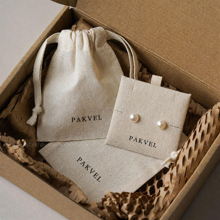 Pearl earrings on a branded linen card inside a kraft gift box with drawstring pouch and honeycomb wrap
